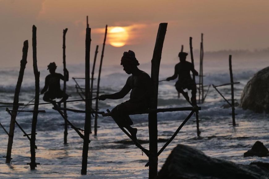 Silhouettes of fishermen on stilts on the beach at sunset.