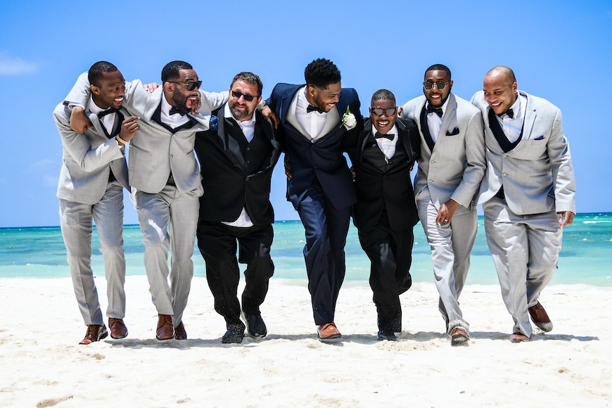 A group of groomsmen walking on the beach.