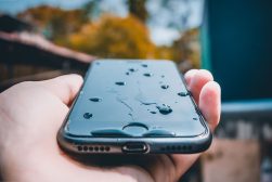 A person holding an iphone with water drops on it.