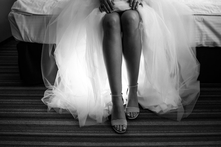 A bride in a wedding dress sitting on a bed showing her feet