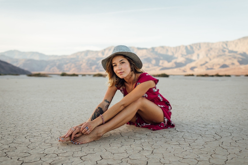 A woman in a hat sitting on the ground in the middle of a desert.