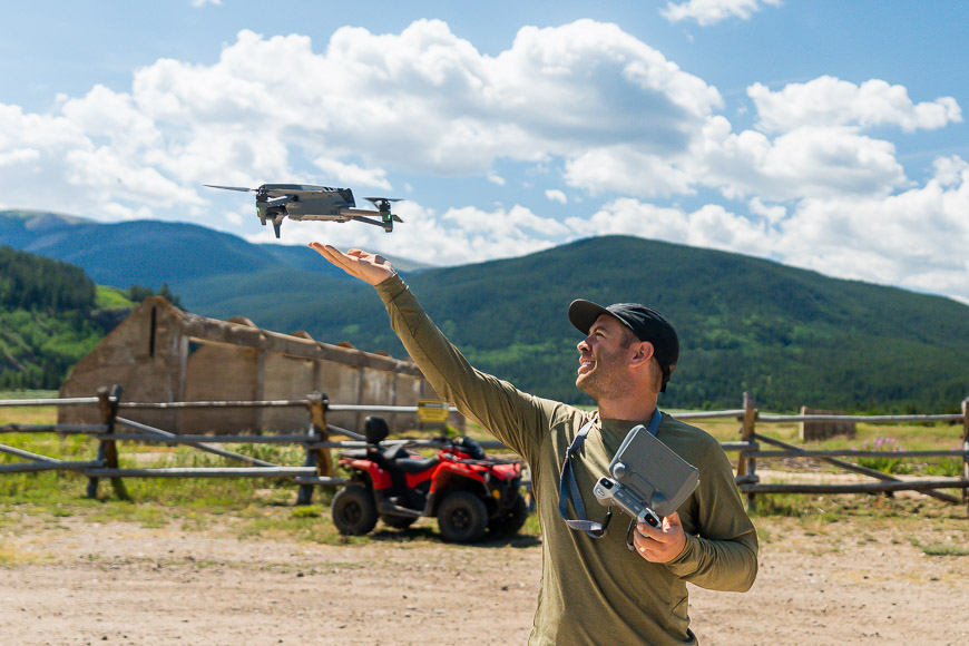A man is holding a drone in front of a field.