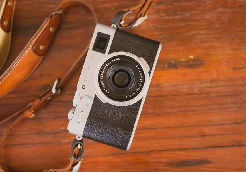 A camera with a leather strap on a wooden table.