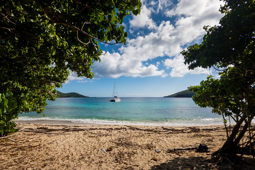 A sandy beach with a sailboat in the water.