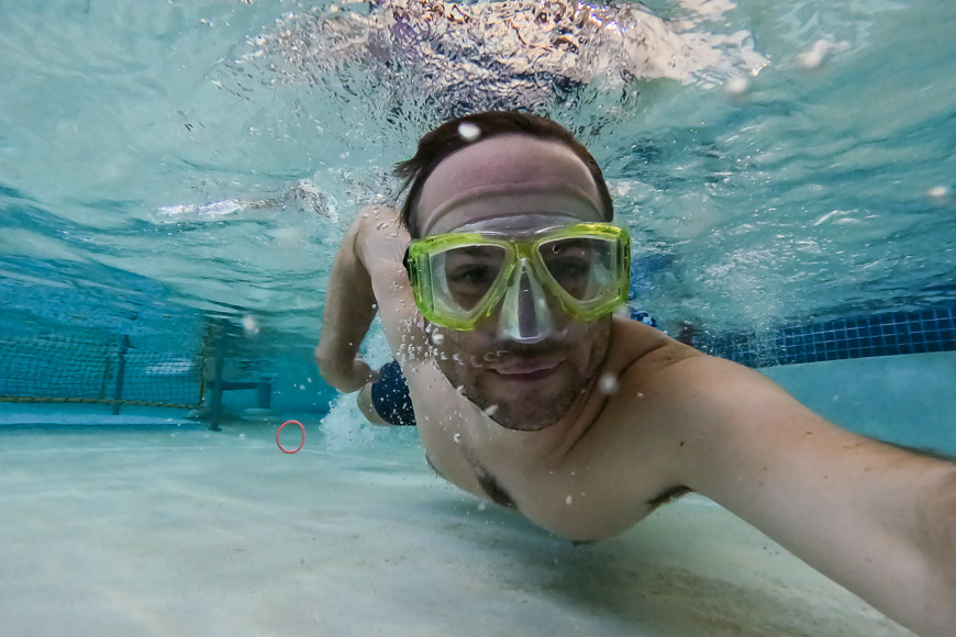 A man wearing a goggles underwater in a swimming pool.