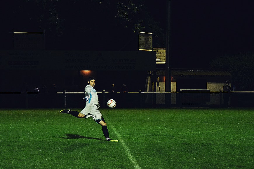 A man kicking a soccer ball at night.