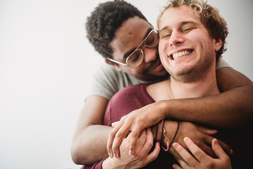 Two gay men hugging each other in front of a white wall.