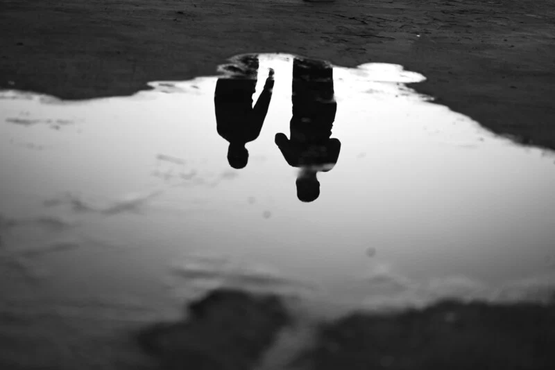 A black and white photo of two people standing in a puddle.