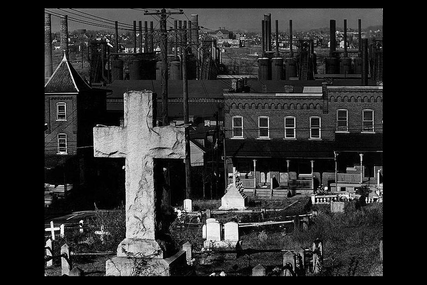 A black and white photo of a cemetery with a cross.