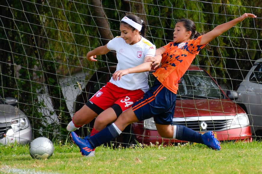 Two female soccer players are fighting for the ball.