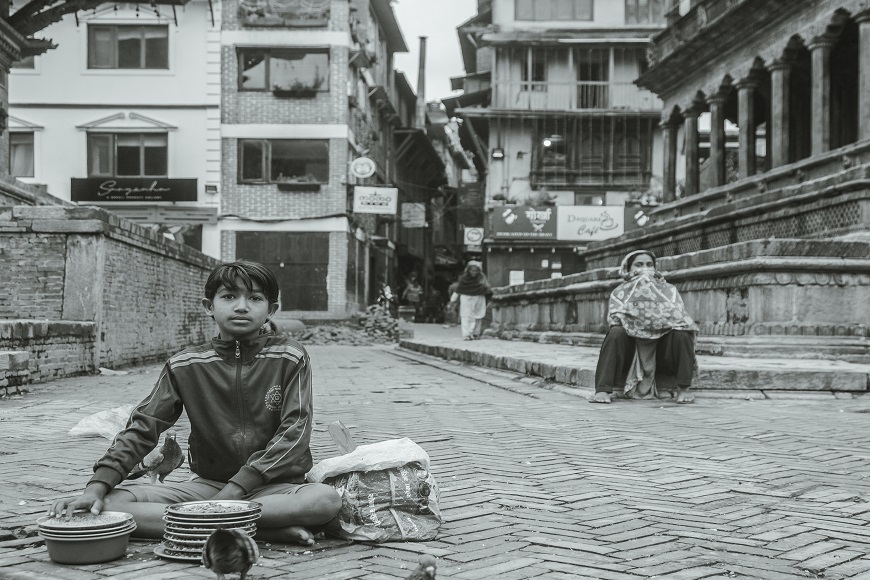 A boy sits on a brick street in nepal.