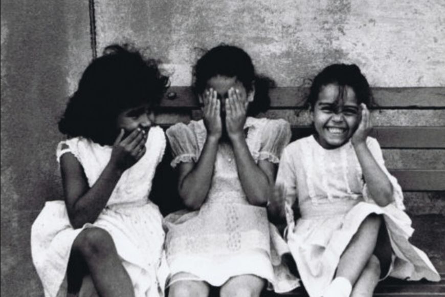 Three girls sitting on a bench with their faces covered.