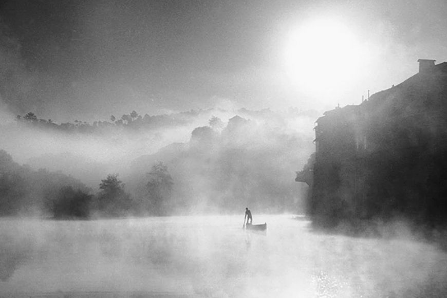 A black and white photo of a man in a canoe on a lake.