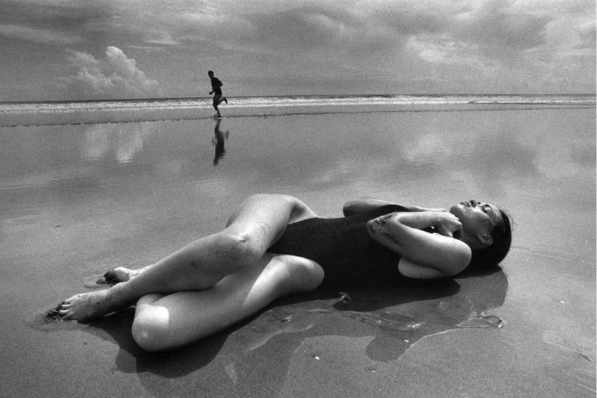 A black and white photo of a woman laying on the beach.