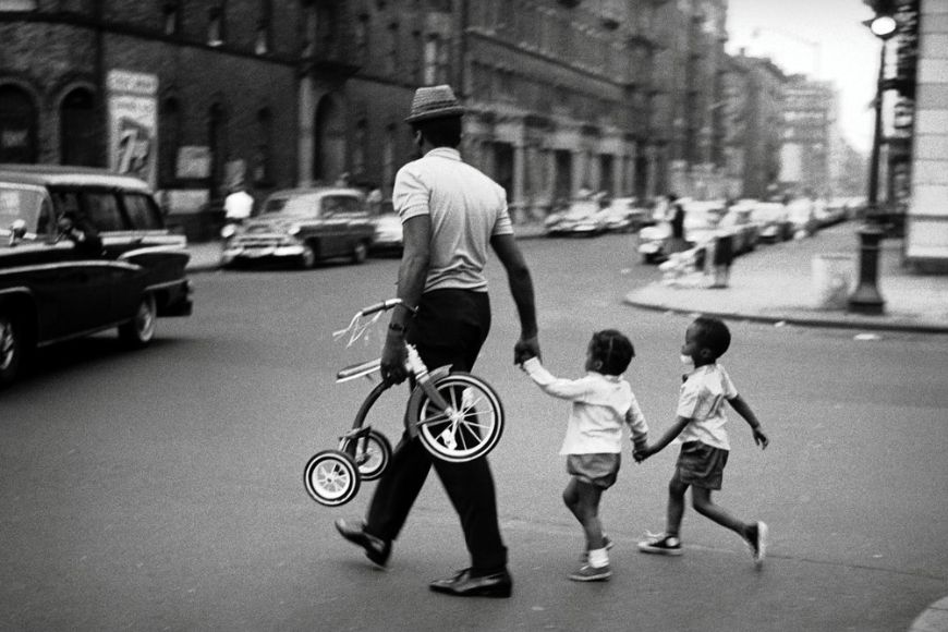 An old black and white photo of a man and his children walking down the street.