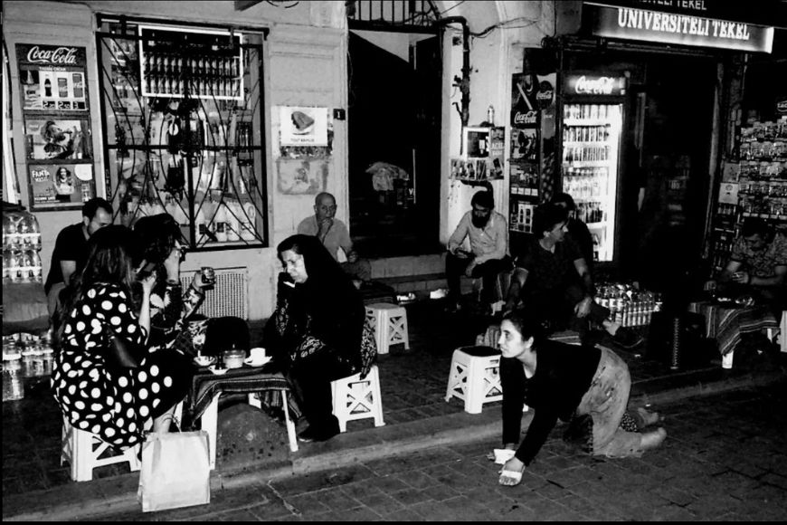 Black and white photo of a group of people sitting on a sidewalk.