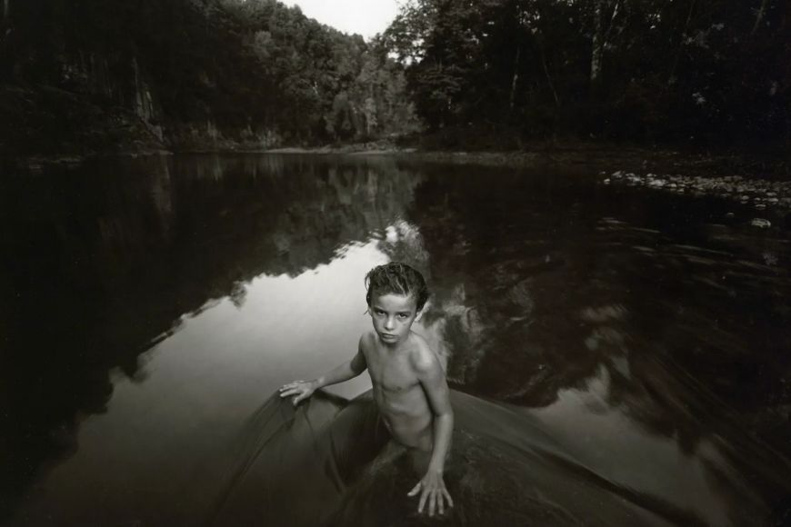 A black and white photo of a boy in a river.