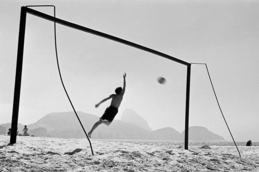 A black and white photo of a man playing volleyball on the beach.