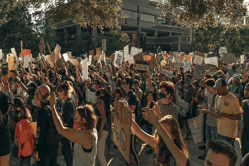 Crowd of people participating in a protest, holding signs and using smartphones.