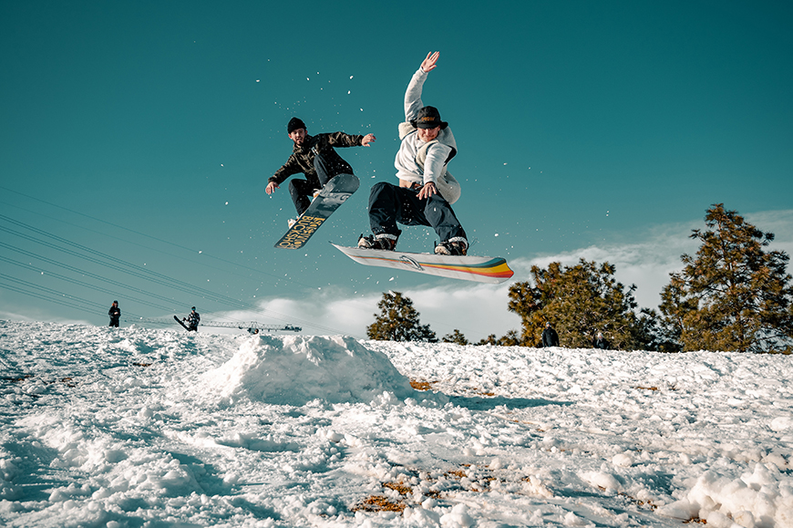 Two people in the air doing a snowboard trick.