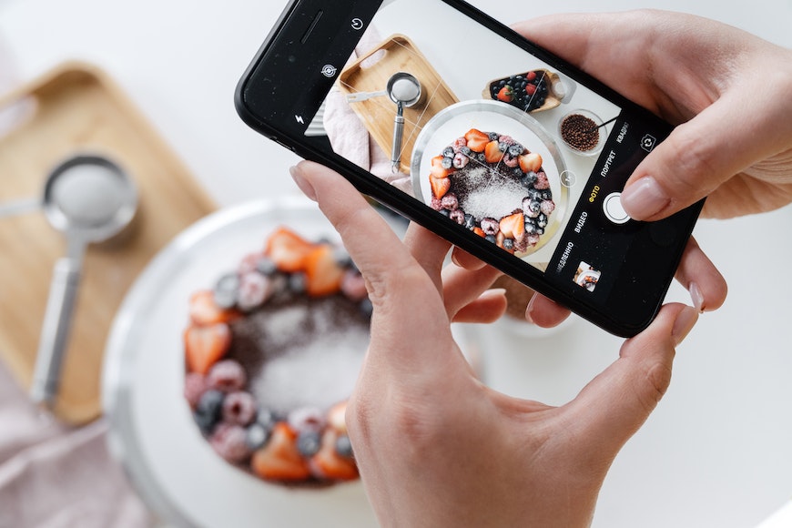 A person taking a photo of a cake on a smartphone.
