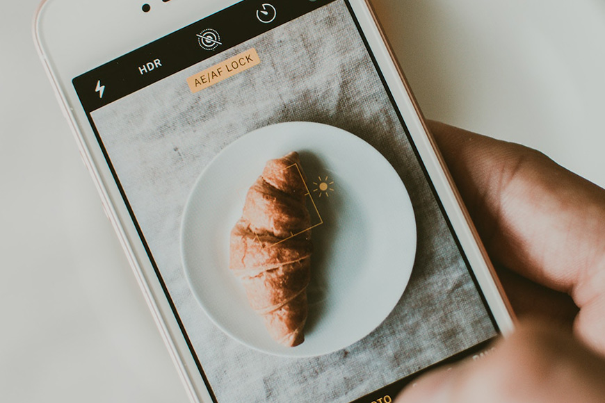A person taking a photo of a croissant on a phone.