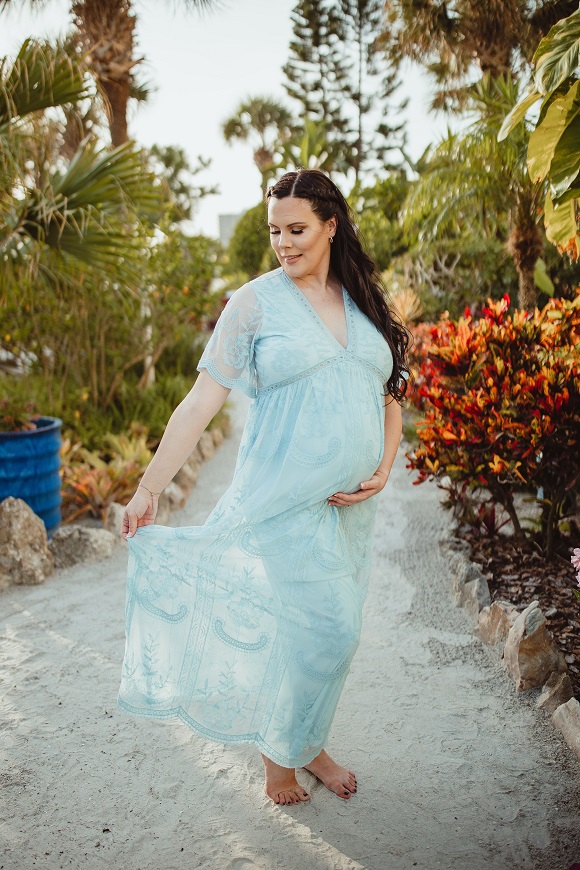 A pregnant woman in a blue dress poses in front of a palm tree.