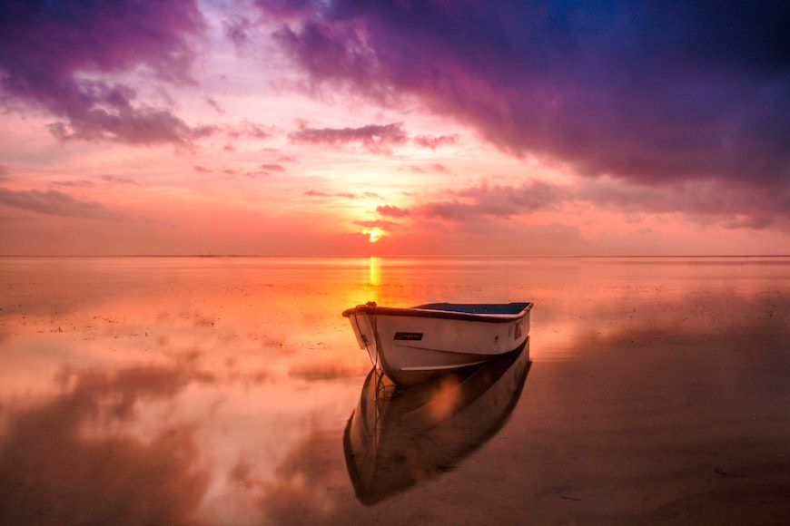 A boat sits on the beach at sunset.