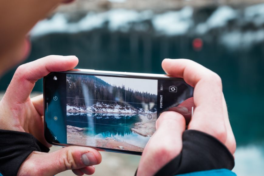 A person taking a picture of a lake with a smartphone.