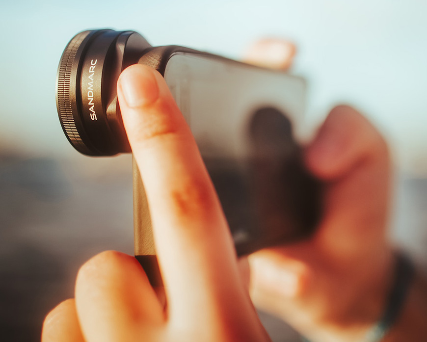 A person holding up a cell phone with a lens attached to it.
