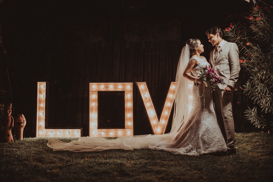 A bride and groom standing in front of a lit up love sign.