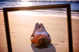 A woman laying on the beach in front of a frame.