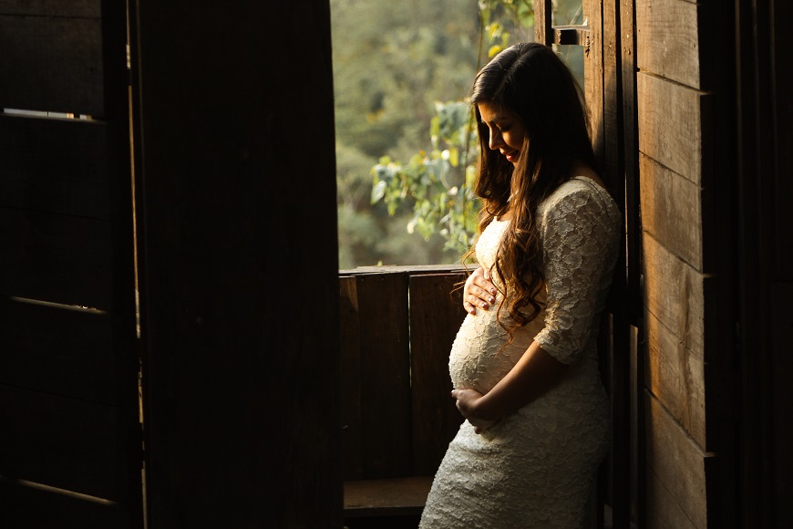 A pregnant woman leaning against a wooden door.