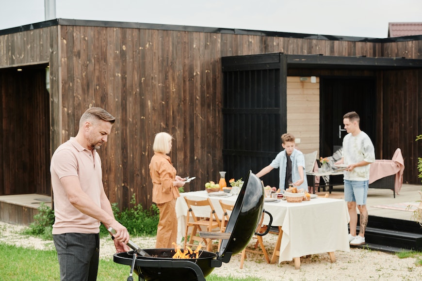 A group of people grilling on a bbq in a backyard.