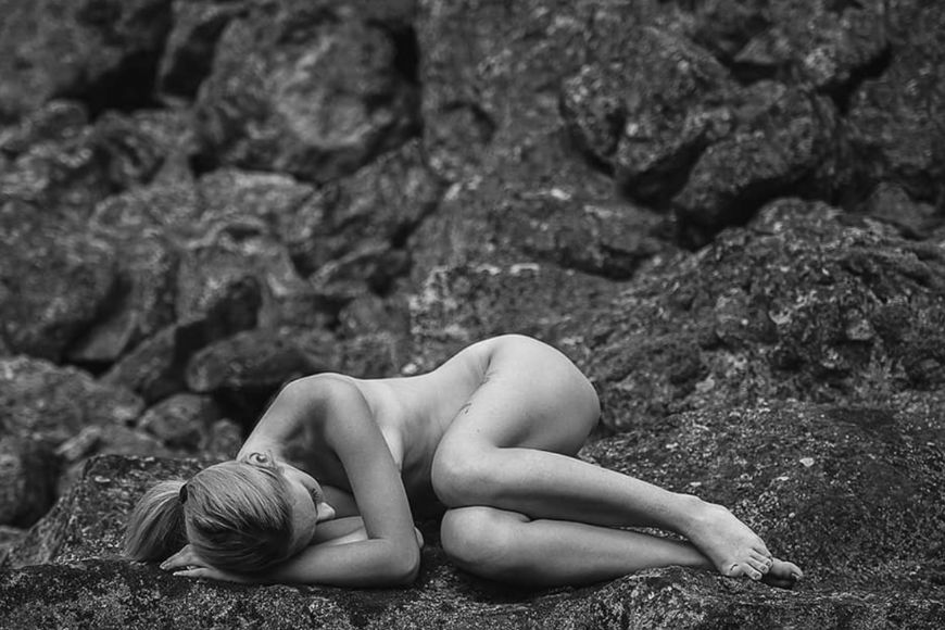 Black and white photo of a naked woman laying on rocks.