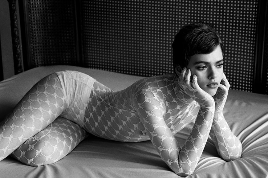 A woman in a white bodysuit laying on a bed.