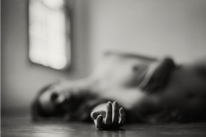 A black and white photo of a naked woman laying on the floor.