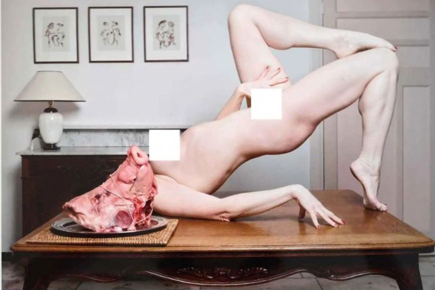 A naked woman laying on a table with a piece of meat on it.