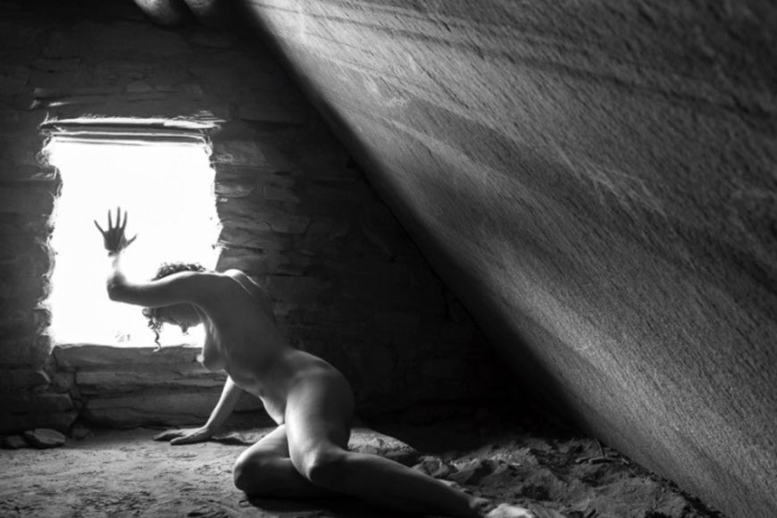 A black and white photo of a naked woman in an attic.