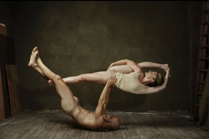 A man and a woman doing acrobatics in a room.