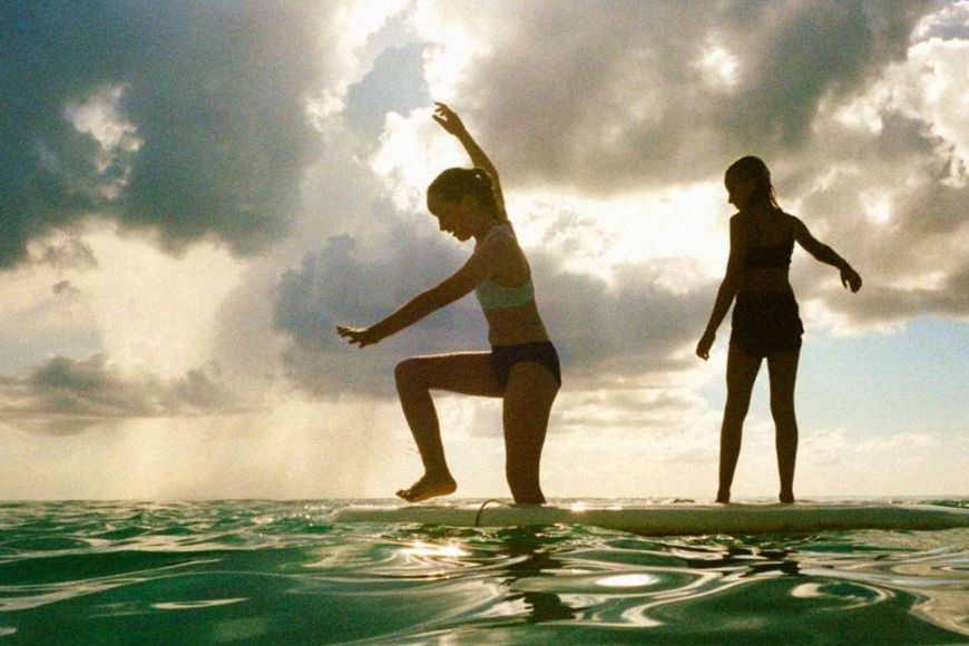 Two women standing on a surfboard in the ocean.