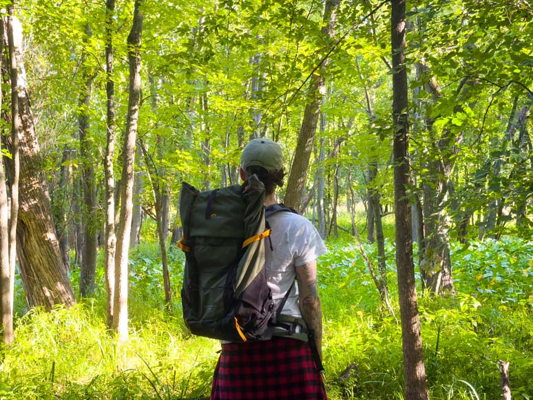 A woman with a backpack walking through a wooded area.