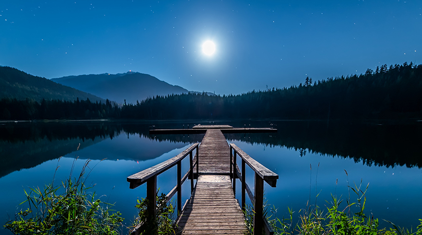 A dock over a lake at night with a full moon.