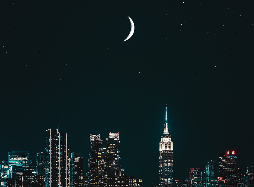 New york city at night with a crescent in the sky.