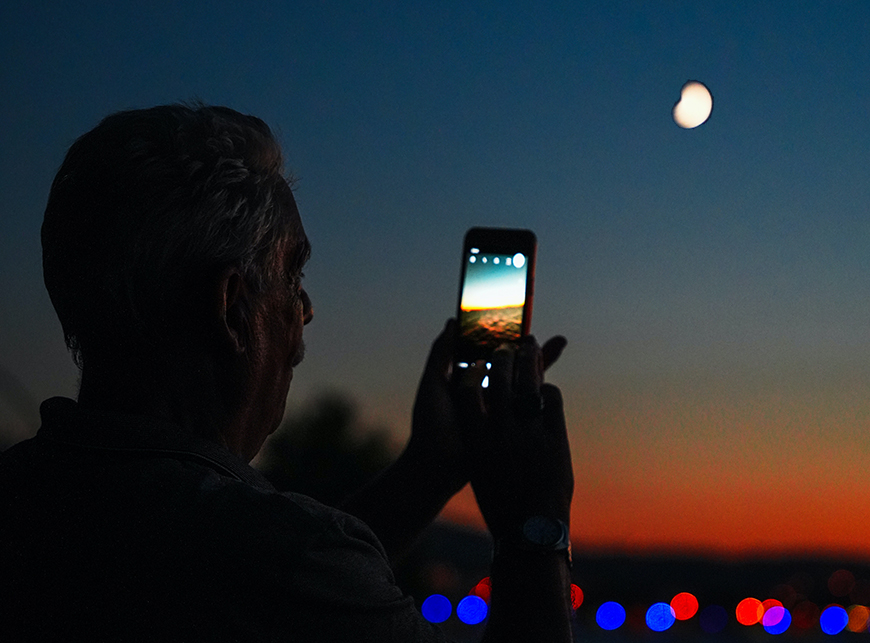A man taking a photo of the moon with his cell phone.