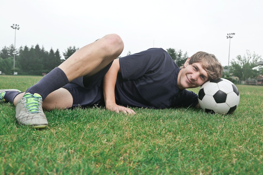 A young man laying on the grass with a soccer ball.