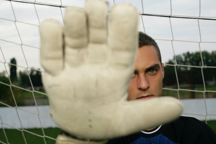 A soccer player is holding his hand up in front of the net.