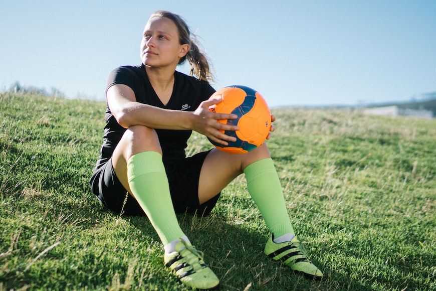 A woman sitting on a grassy hill with a soccer ball.