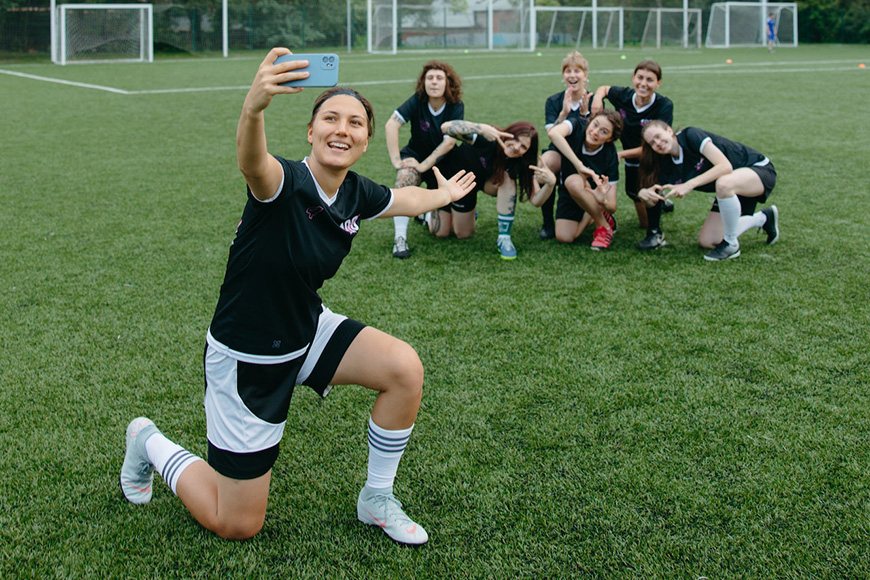 A group of women taking a selfie on a soccer field.
