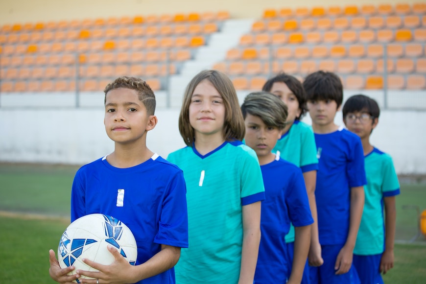 A group of children standing in front of a soccer field.